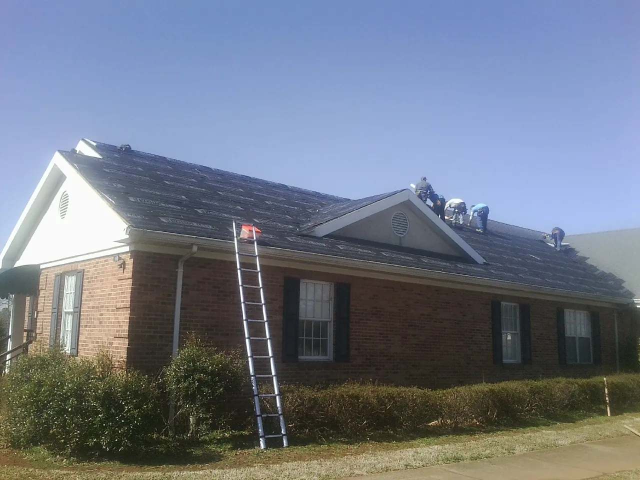 Crew tearing shingles off a brick ranch roof with a ladder set — Emergency Roof Repair work by our crew in Rising Sun