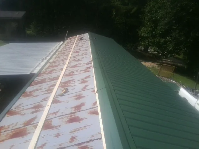 Old rusted panels beside newly installed green metal roofing — Wind Damage Roof Repair by Roofing Brothers in Rising Sun