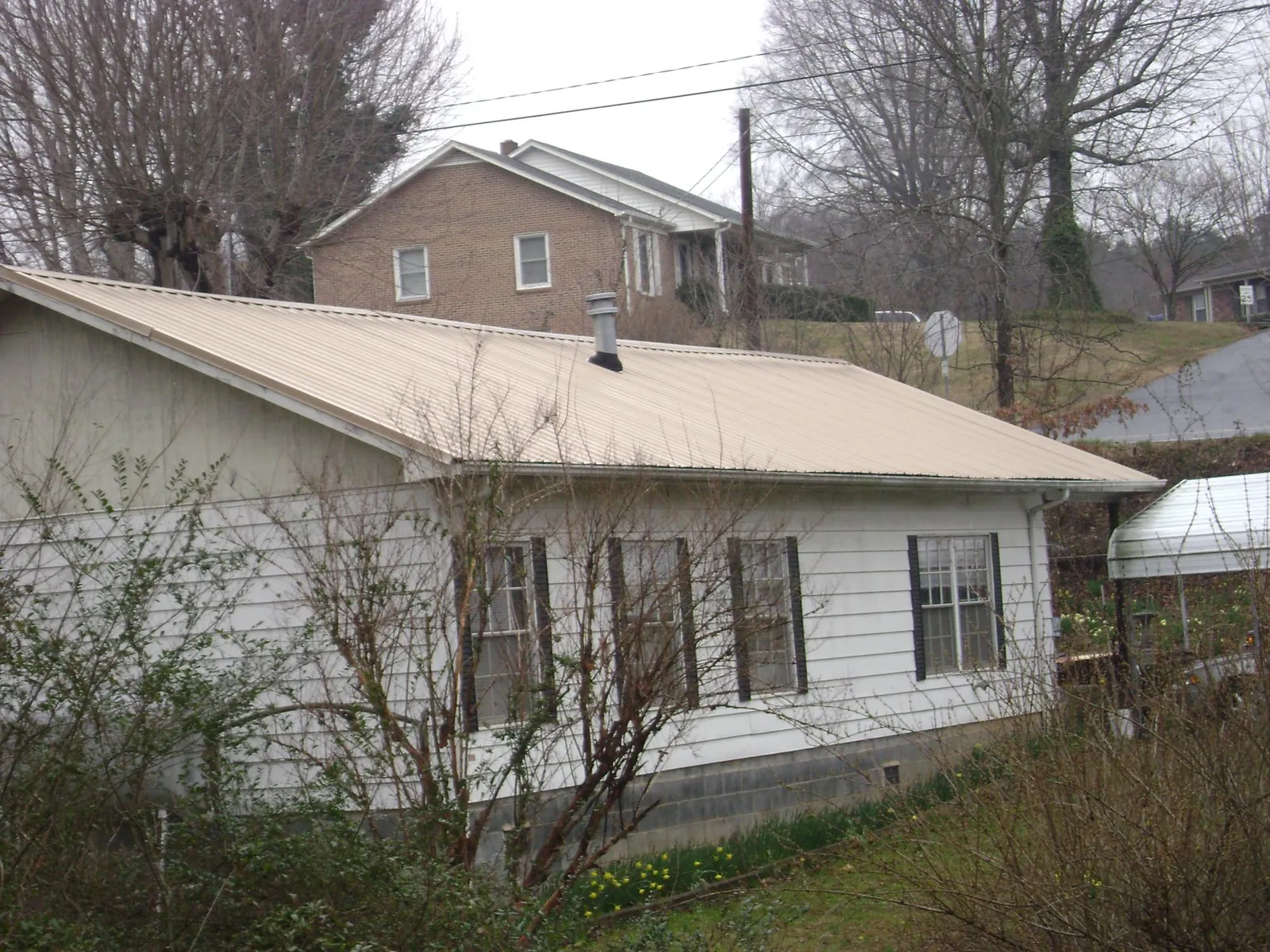 Tan metal roof on a white sided house set into a hillside — Commercial Roofing by Roofing Brothers in Rising Sun